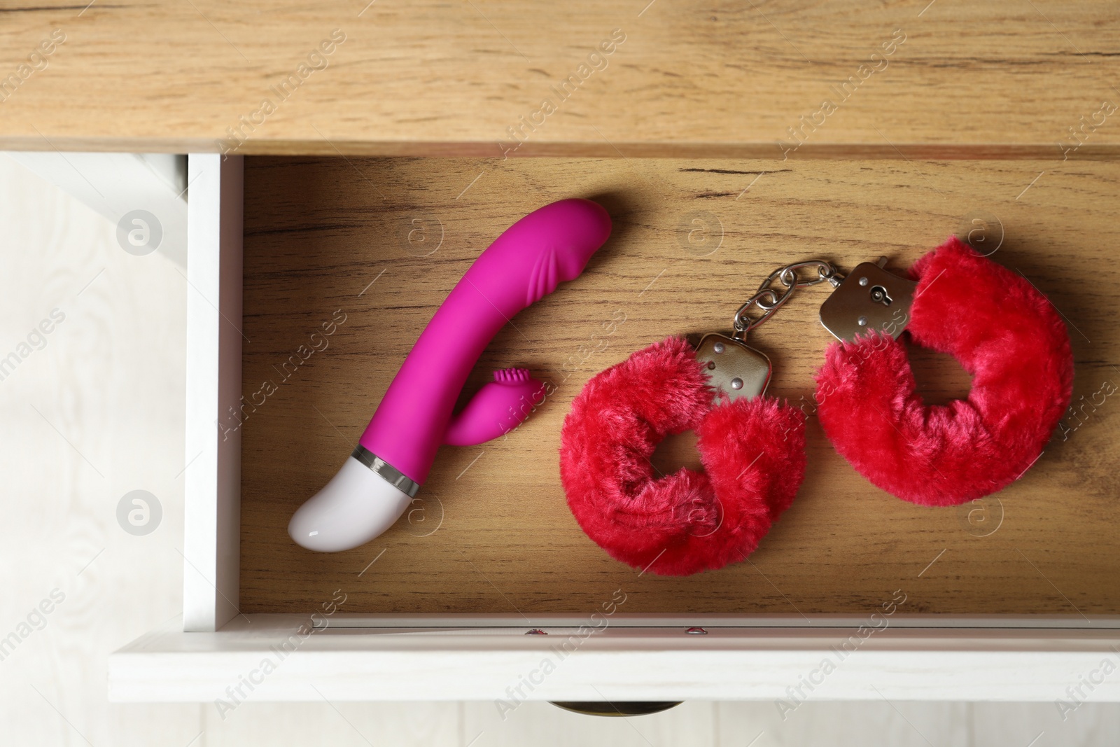 Photo of Fluffy handcuffs and vibrator in open wooden drawer, top view. Sex toys