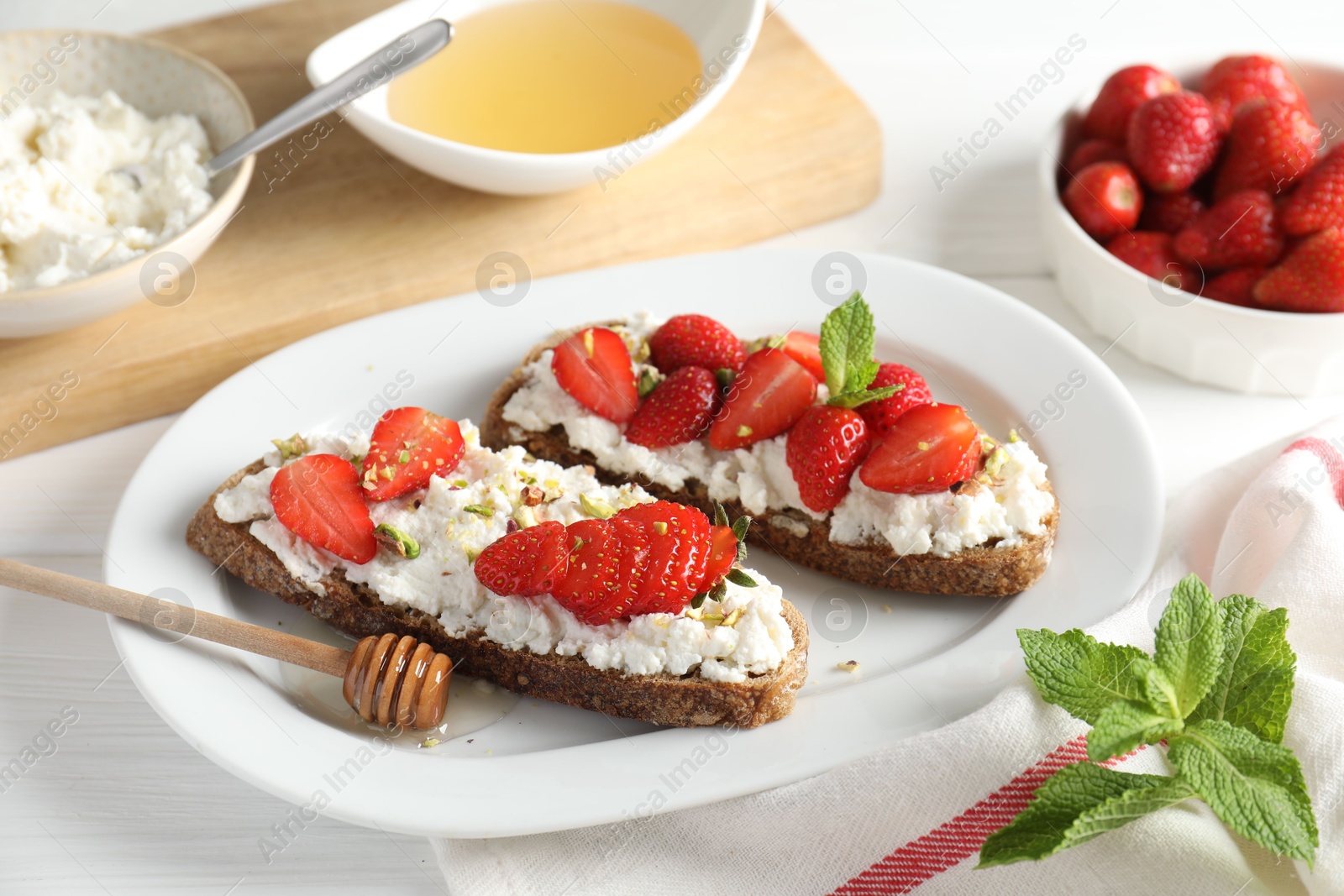 Photo of Delicious ricotta bruschettas with strawberry, mint, pistachios served with honey on white table