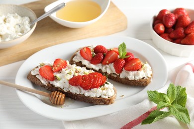 Photo of Delicious ricotta bruschettas with strawberry, mint, pistachios served with honey on white table