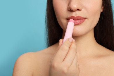 Photo of Young woman applying lip balm on turquoise background, closeup. Space for text