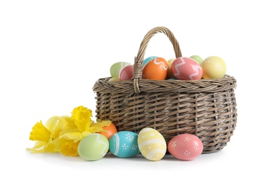 Photo of Wicker basket with painted Easter eggs and spring flowers on white background