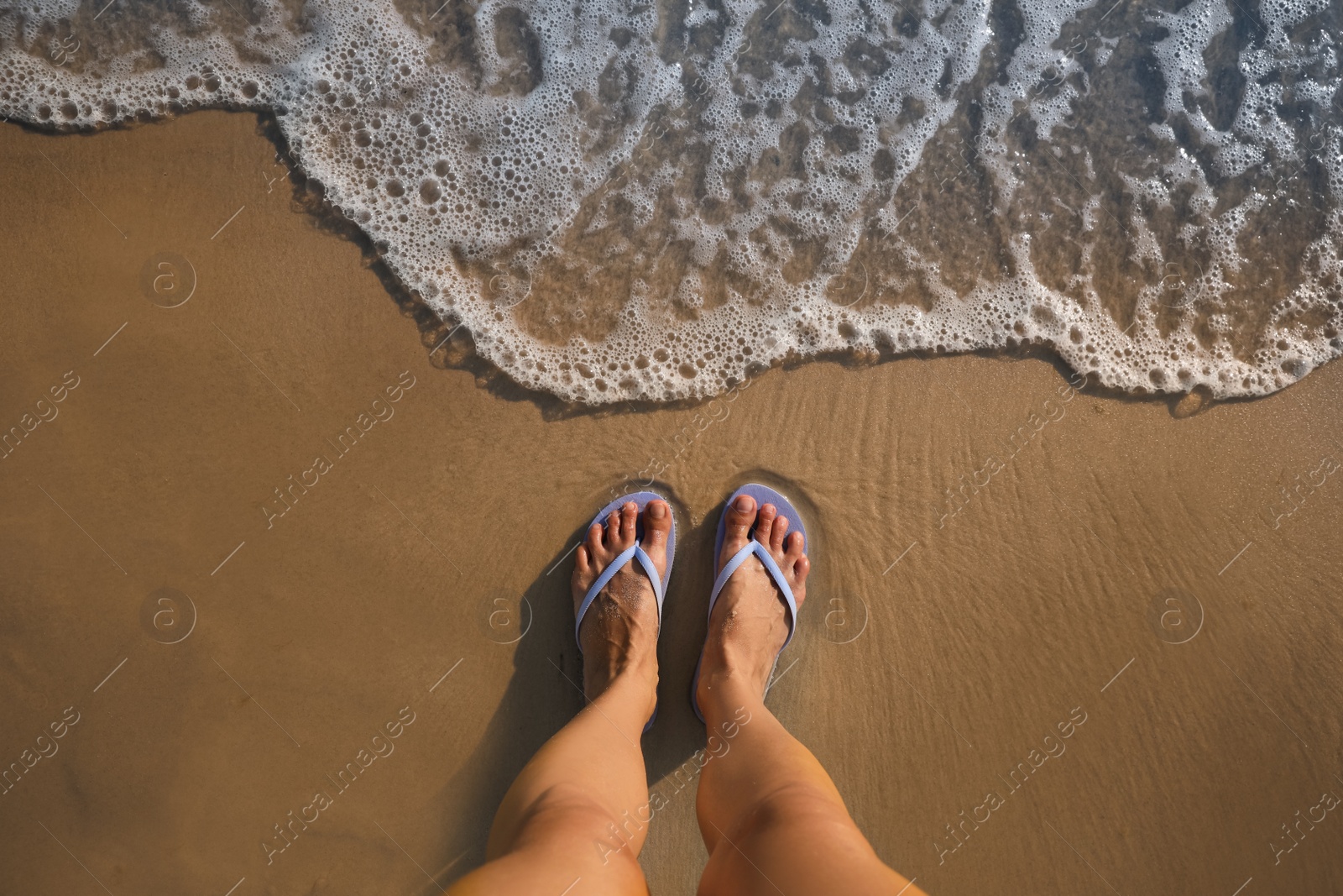 Photo of Top view of woman wearing beach slippers on sandy seashore, closeup