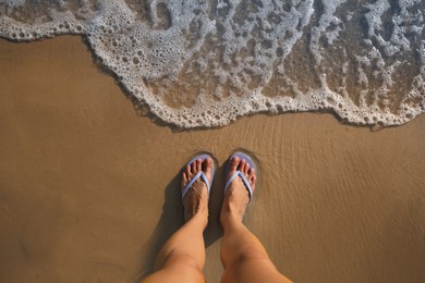 Photo of Top view of woman wearing beach slippers on sandy seashore, closeup