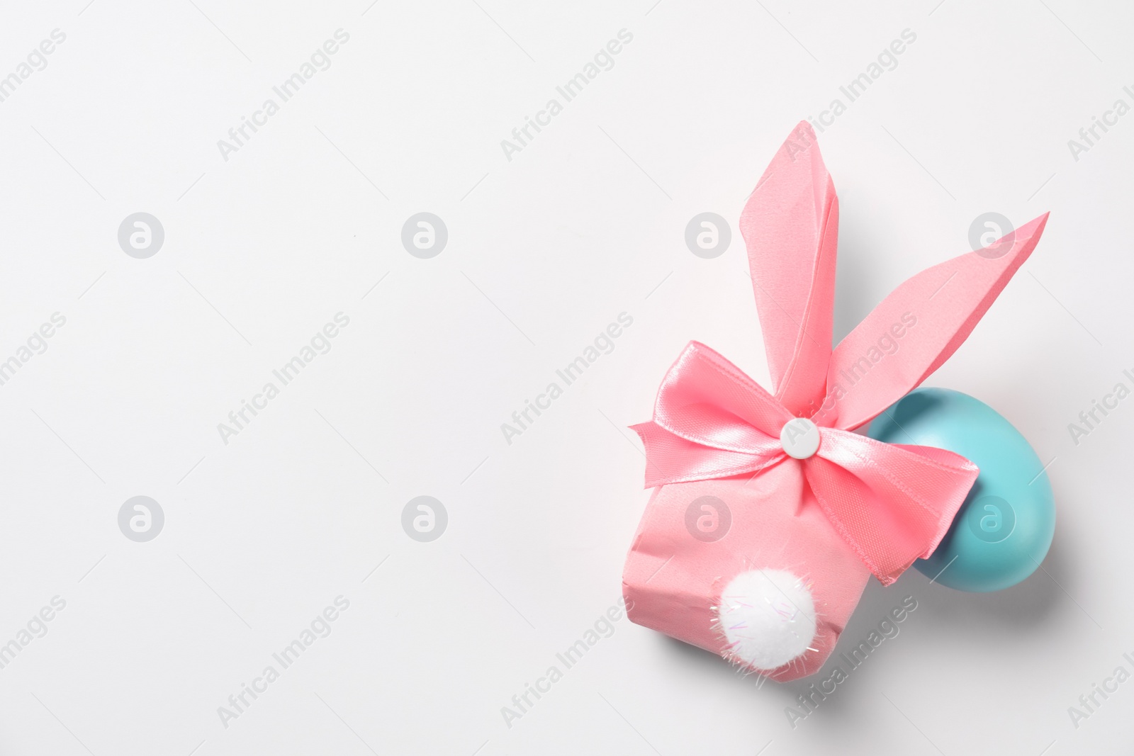 Photo of Easter bunny gift bag and dyed egg on white background, top view