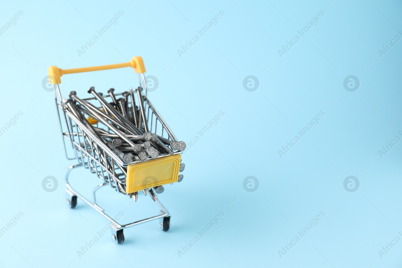 Photo of Metal nails in shopping cart on light blue background, space for text