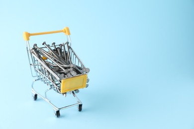 Metal nails in shopping cart on light blue background, space for text