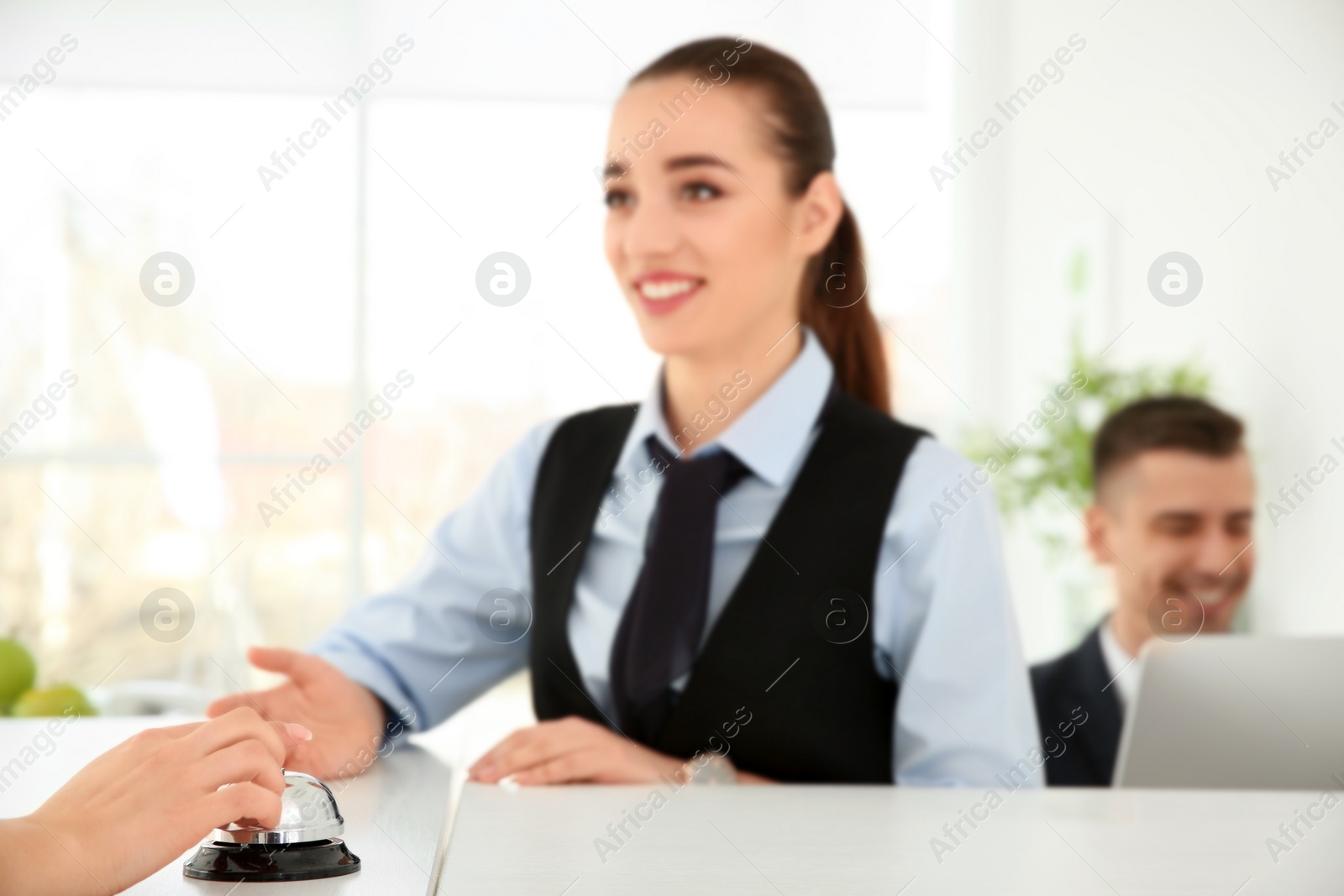 Photo of Young woman ringing service bell on reception desk in hotel