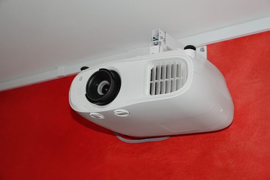 Photo of Modern digital video projector on red wall indoors, closeup