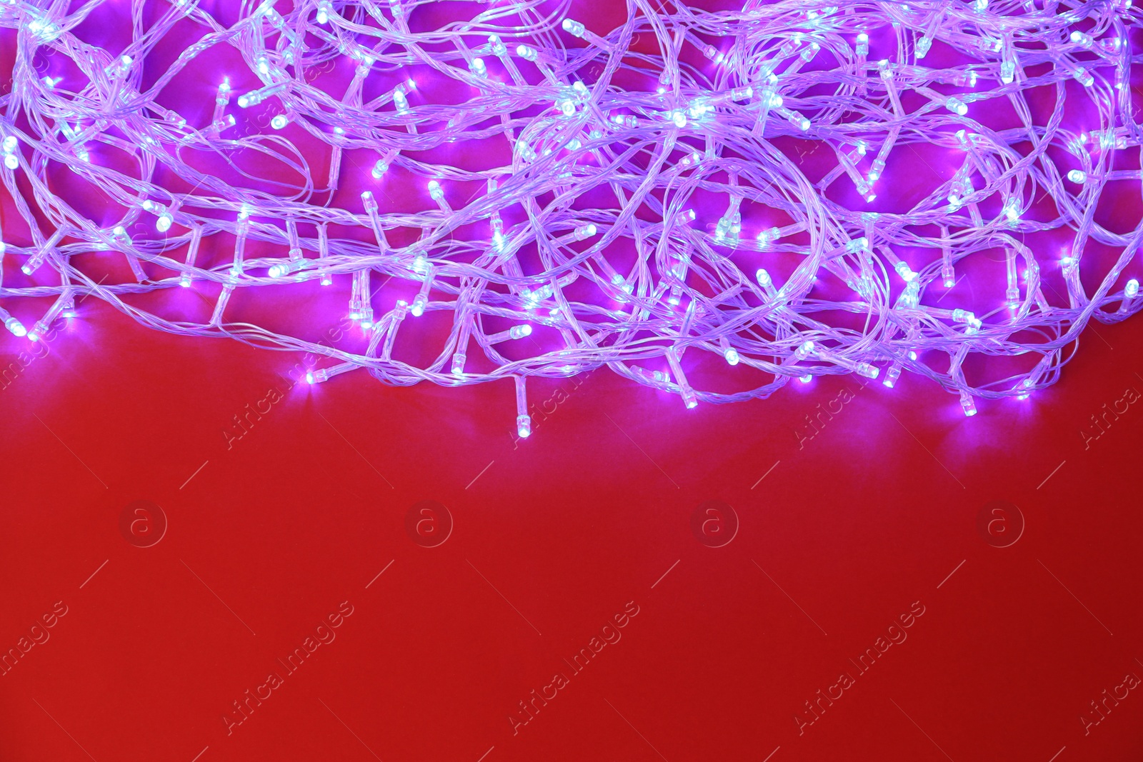 Photo of Glowing Christmas lights on red background, top view. Space for text