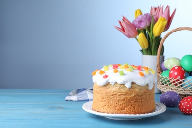Photo of Easter cake, colorful eggs and tulips on light blue wooden table, space for text