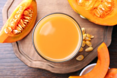 Photo of Tasty pumpkin juice in glass and cut pumpkin on wooden table, flat lay