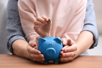 Photo of Couple with piggy bank and coin at wooden table, closeup