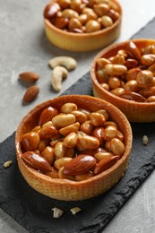 Photo of Tartlets with caramelized nuts on light grey table, closeup. Tasty dessert