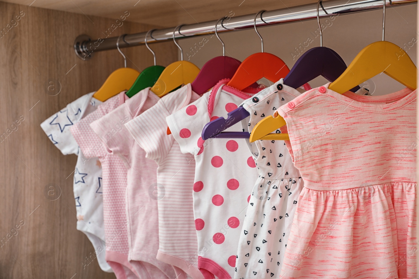 Photo of Hangers with baby clothes on rack in wardrobe, closeup