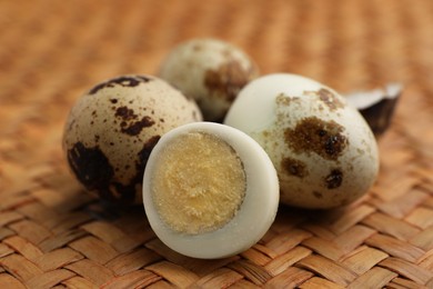 Unpeeled and peeled hard boiled quail eggs on wicker surface, closeup