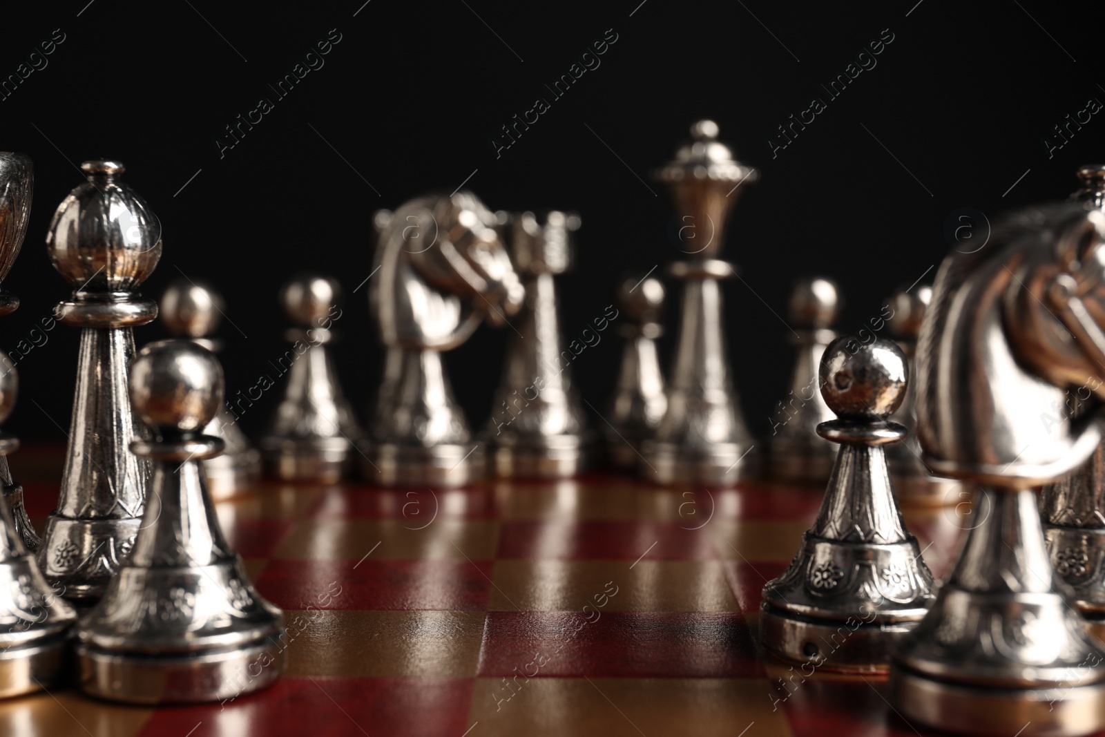 Photo of Many chess pieces on wooden checkerboard against black background, selective focus