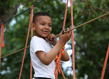 Photo of Little African-American boy climbing in adventure park. Summer camp