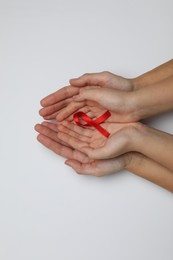 Photo of Woman and girl holding red ribbon on white background, top view. AIDS disease awareness