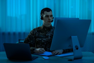 Military service. Soldier in headphones working at wooden table in office at night