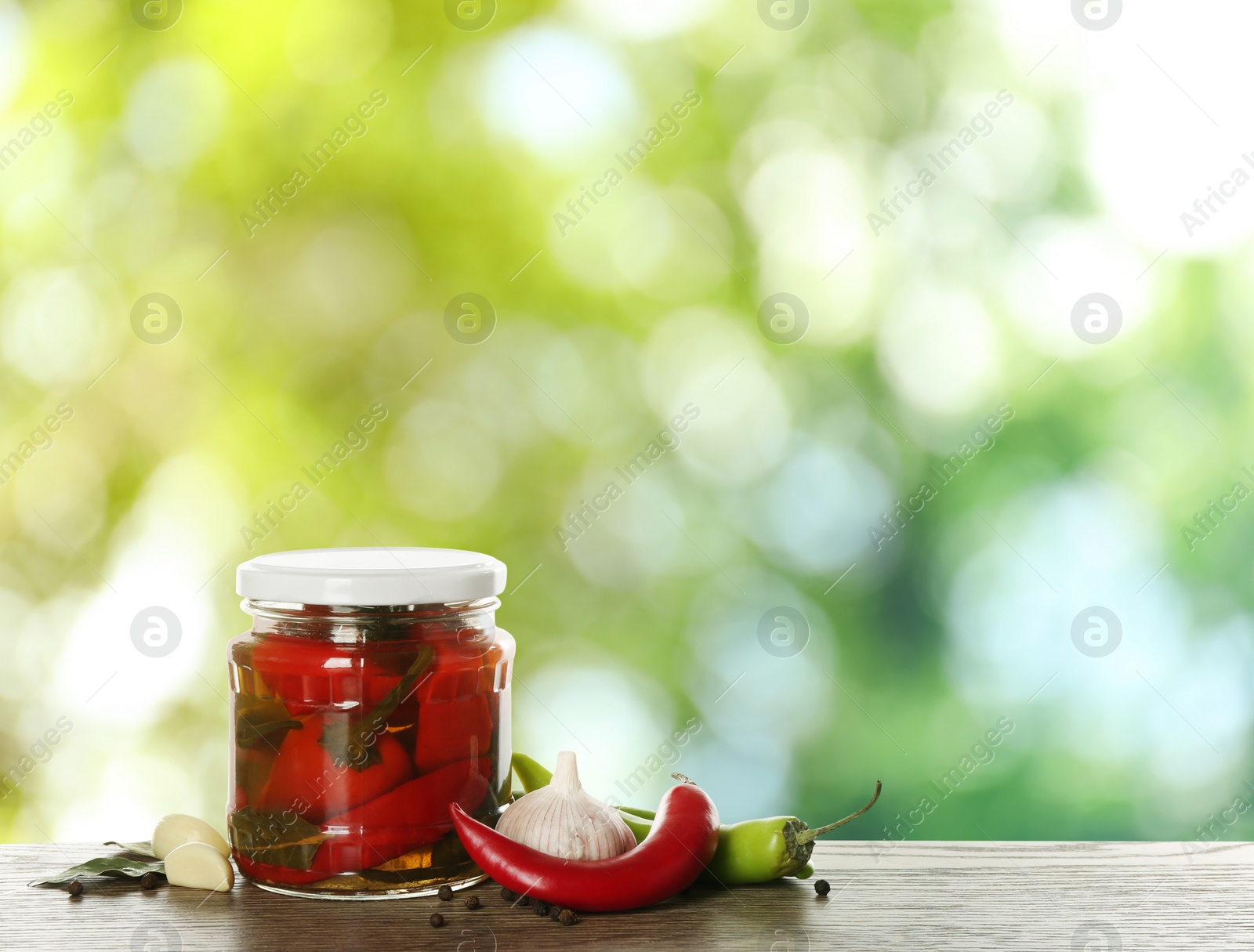 Image of Jar of tasty pickled chili peppers on wooden table against blurred green background. Space for text