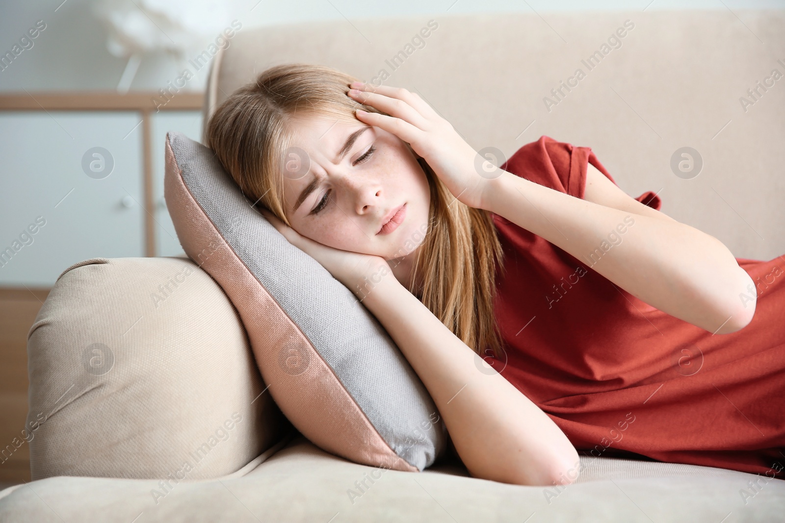 Photo of Teenage girl suffering from headache while lying on couch at home