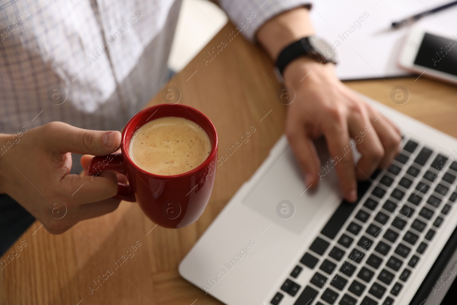 Photo of Man with cup of coffee and laptop at workplace, closeup