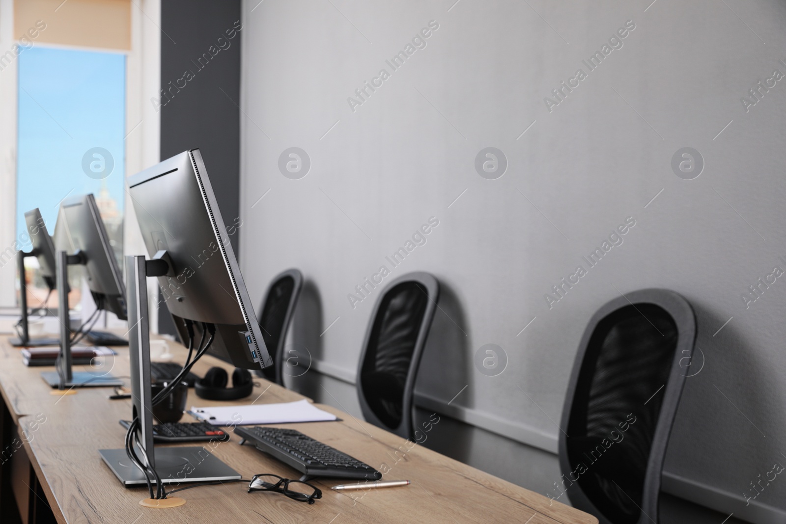 Photo of Open office interior. Modern workplaces with computers near light grey wall