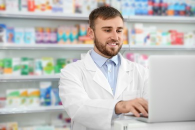 Professional pharmacist working on laptop in modern drugstore