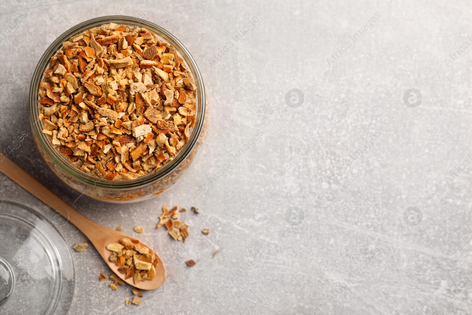 Photo of Jar and spoon with dried orange zest seasoning on light grey table, flat lay. Space for text