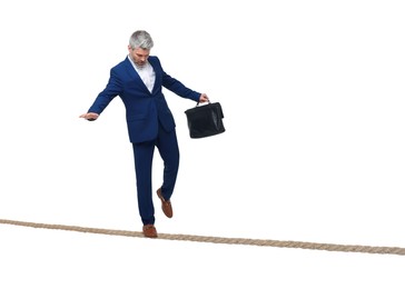 Image of Risks and challenges of owning business. Man with briefcase balancing on rope against white background