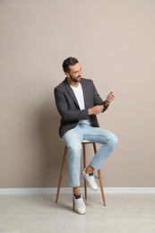 Photo of Handsome man sitting on stool near beige wall