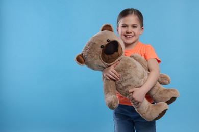 Photo of Cute girl with teddy bear on light blue background, space for text