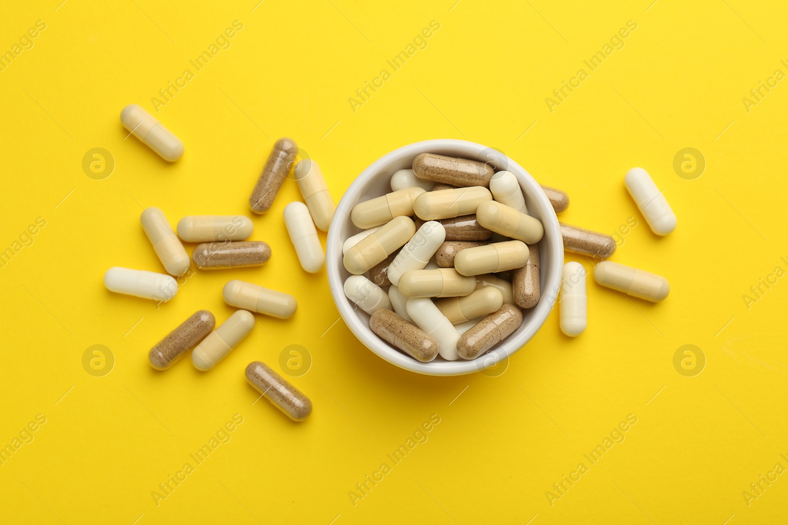 Photo of Different vitamin capsules on yellow background, flat lay