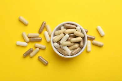 Photo of Different vitamin capsules on yellow background, flat lay