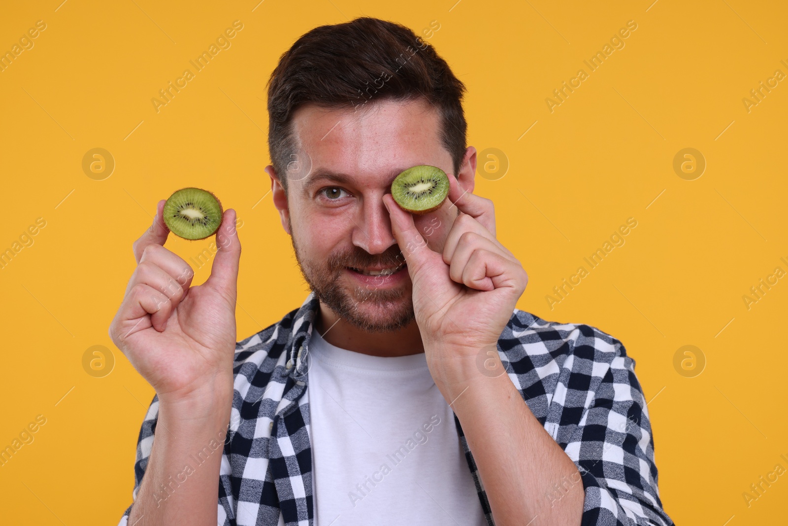 Photo of Man holding halves of kiwi on yellow background