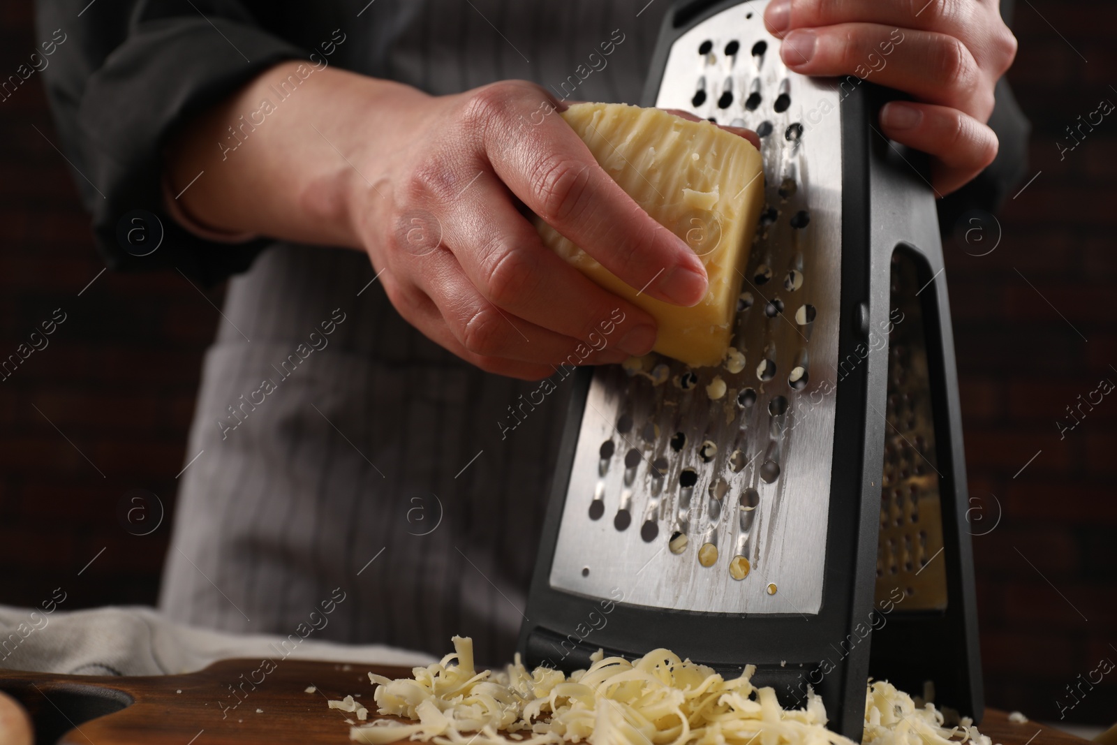 Photo of Woman grating cheese at wooden table, closeup