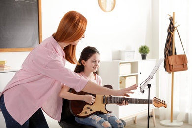 Photo of Little girl playing guitar with her teacher at music lesson. Learning notes