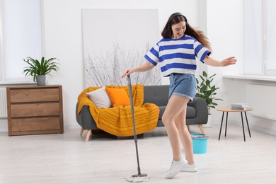 Photo of Enjoying cleaning. Happy woman in headphones dancing with mop at home. Space for text
