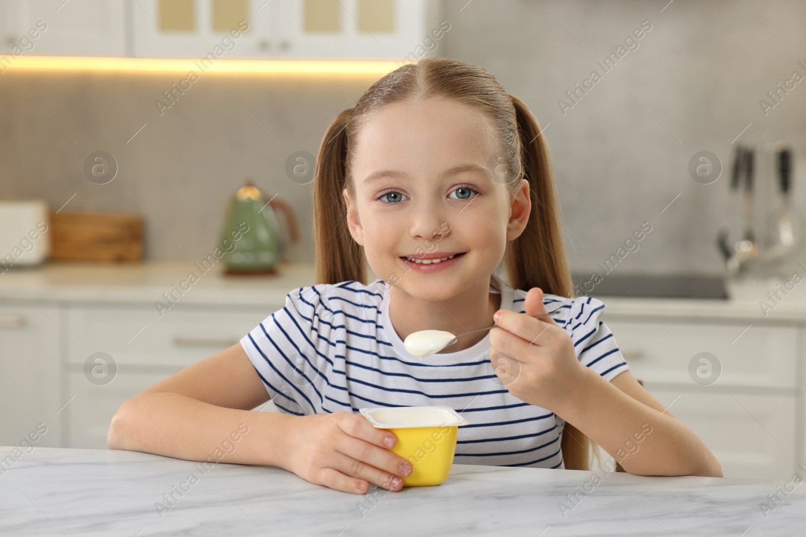 Photo of Cute little girl with tasty yogurt at white marble table in kitchen