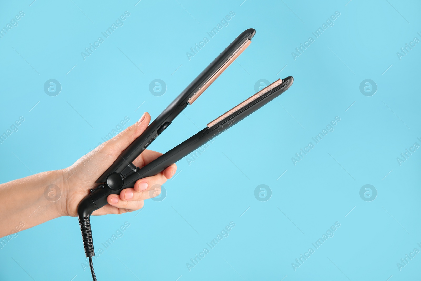 Photo of Woman holding corrugated hair iron on light blue background, closeup