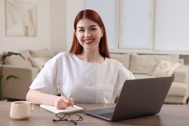 Happy woman with notebook and laptop at wooden table in room