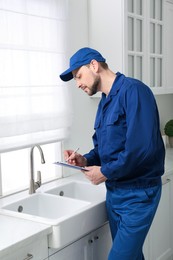 Professional plumber with clipboard checking water tap in kitchen