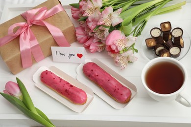 Photo of Tasty breakfast served in bed. Delicious desserts, tea, flowers, gift box and card with phrase I Love You on tray, above view