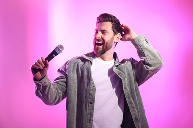 Photo of Handsome man with microphone singing on pink background