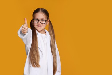 Photo of Little girl in medical uniform showing thumb up on yellow background. Space for text