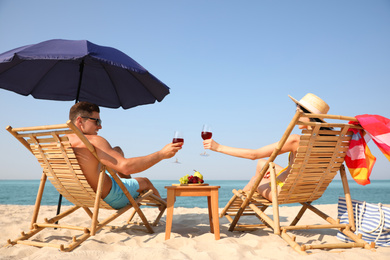 Photo of Happy couple with wine on sunny beach at resort