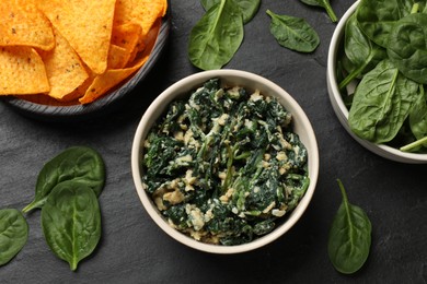 Photo of Tasty spinach dip with egg in bowl and nachos chips on black table, flat lay