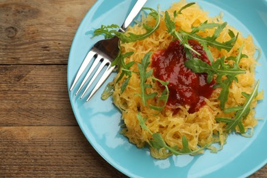 Photo of Tasty spaghetti squash with tomato sauce and arugula served on wooden table, top view