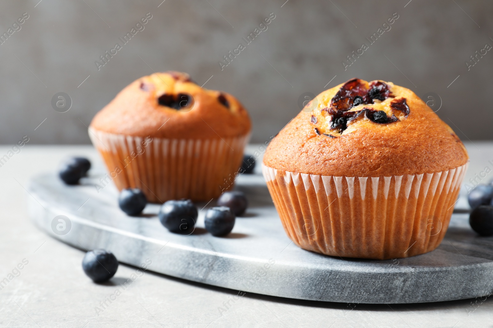 Photo of Stone board with blueberry muffins on light table, closeup view. Space for text