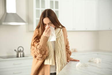 Photo of Sick young woman sneezing in kitchen. Influenza virus